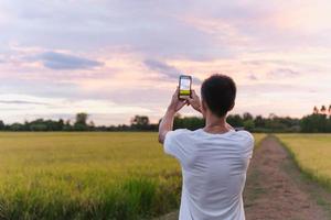 Tourist man taking picture of rice field at sunset with cell phone.