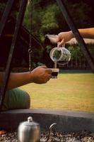 Hand pouring coffee with kettle on setting of bonfire at camping. photo