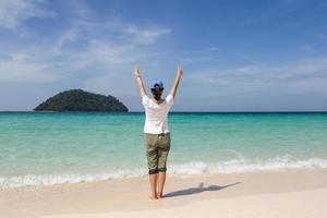 Back view of woman with hands raised up at the beach. photo