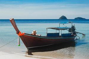 mujer no identificada sentada en un bote de madera tomando el sol en el mar.