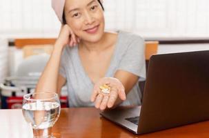 Woman holding pills while working on laptop at home. photo