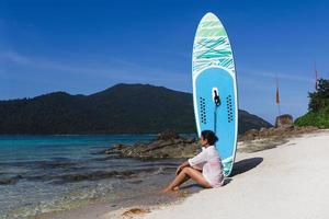 Female surfer with tanned skin sitting on beach with paddle board. photo
