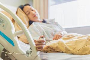 Woman patient holding emergency call button while lying in hospital  bed.