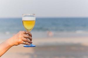 Woman holding a glass of beer on the beach.