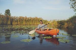 asian younger woman sailing sea kayak in lotus flower lagoon with happiness