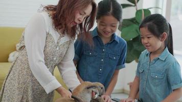 madre asiática y niños jugando con conejo marrón juntos en casa