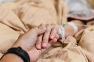 Husband hand holding his wife hand on bed in hospital room.