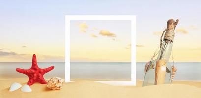 marco de papel cuadrado blanco sobre arena de playa rodeado de estrellas de mar, conchas y mensaje en la botella. copie el espacio en el medio foto
