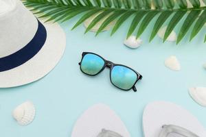 accesorios de playa de verano sobre fondo azul. sombrero, anteojos, pantuflas, conchas y hojas de palma foto