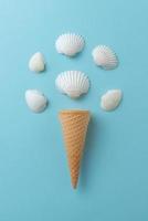 Shellfish ice cream concept on blue surface. Ice cream cone with white shells. photo
