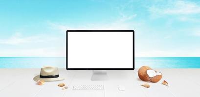 Computer display mockup on desk with beach in background. Isolated screen for mockup. Traveler hat, coconuts and shells beside. Travel concept photo