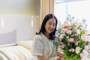 Woman patient smiling and holding a flower bouquet sitting on hospital bed. photo