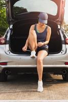 retrato de una mujer atándose los cordones de los zapatos mientras se sienta en el maletero de su coche. foto