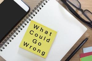 texto en una nota amarilla con un bloc de notas en un escritorio de madera: ¿qué podría salir mal? foto