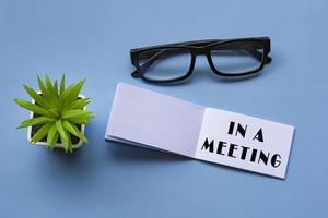 In a meeting text on notepad with reading glasses and potted plant. photo