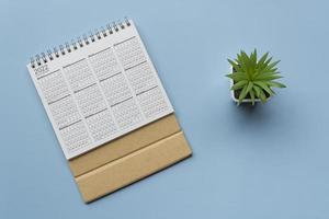 2022 white calendar with potted plant on blue background. Flat lay photo