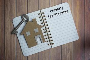 texto de planificación de impuestos sobre la propiedad en un cuaderno con modelo de casa y llave en un escritorio de madera foto