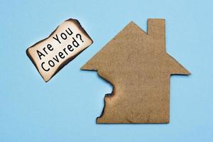 Text on burned paper house model on blue background. Home insurance concept. photo