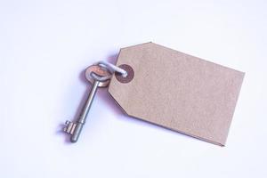 Key and brown paper tag on white background. Flat lay photo