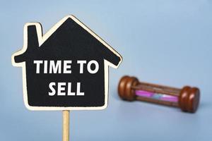 Time to sell text on wooden house with background of hourglass. photo