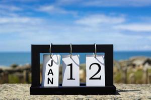 Texto de la fecha del calendario del 12 de enero en un marco de madera con un fondo borroso del océano foto