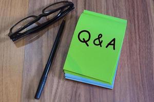 Q and A with punctuation mark text on green notepad with glasses and pen on a desk photo