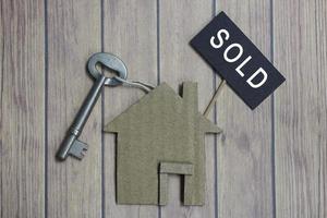 Sold text on dark paper with house model and key on wooden desk photo