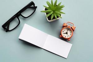 Notepad with reading glasses, pen and alarm clock on blue background. photo