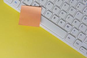 Orange sticky note on top of white keyboard. Flat lay. Copy space. photo