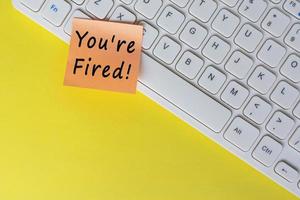 You're Fired text on orange sticky note on top of white keyboard. photo