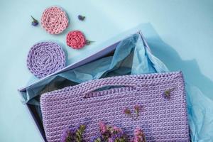 Handmade purple knitted bag in a paper box on a blue background photo
