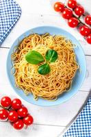 Boiled spaghetti with cherry tomatoes on a white wooden table. Top view