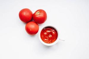 Top view of tomato sauce in a cup and tomatoes around. White background photo
