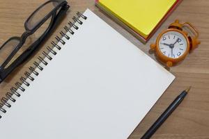 Notepad with yellow note, study glasses, pen and alarm clock. Flat lay photo