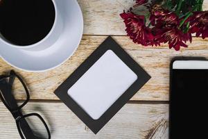 Chalkboard frame with dahlia flowers, white coffee cup and smartphone on wooden desk. Directly above, flat lay, copy space. photo