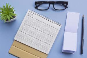 bloc de notas con calendario 2022, gafas, bolígrafo y maceta en un escritorio. endecha plana foto