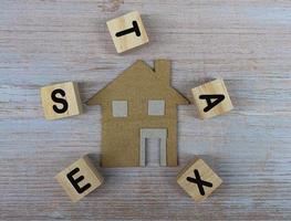 Paper House Model Near Wooden Blocks With Taxes Text On Wooden Background photo