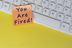 You're Fired text on orange sticky note on top of white keyboard. photo