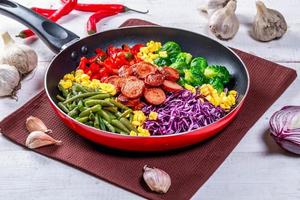 Asparagus, Brussels sprouts, corn, peppers and sausages in a frying pan photo