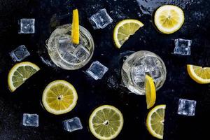 Lemonade with ice cubes and sliced lemon on black background. Top view photo