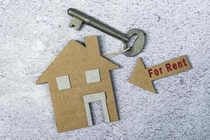 For rent text on brown arrow and paper house model with key on floor tiles
