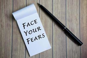 enfréntate al texto de tus miedos en el bloc de notas con un bolígrafo en un escritorio de madera.