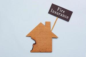 Fire Insurance text on burned paper house model on blue background photo