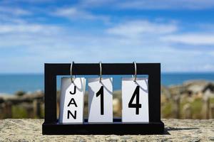 Texto de la fecha del calendario del 14 de enero en un marco de madera con un fondo borroso del océano foto