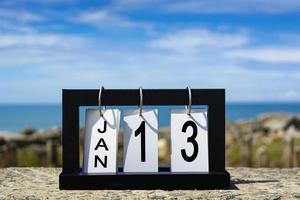 13 de enero texto de fecha de calendario en marco de madera con fondo borroso del océano foto