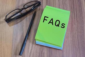 Texto de preguntas frecuentes en el bloc de notas verde con gafas y bolígrafo en un escritorio foto
