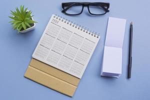 bloc de notas con calendario 2022, gafas, bolígrafo y maceta en un escritorio. endecha plana foto