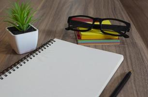 bloc de notas con gafas, bolígrafo, nota de palo de colores y planta en maceta en el escritorio de madera foto