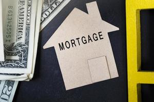 Mortgage text on brown paper house model with dollar banknotes on dark wooden table photo