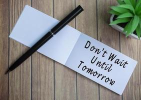 Do not wait until tomorrow text on notepad with potted plant on a wooden desk photo